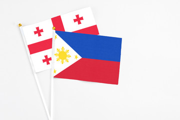 Philippines and Georgia stick flags on white background. High quality fabric, miniature national flag. Peaceful global concept.White floor for copy space.