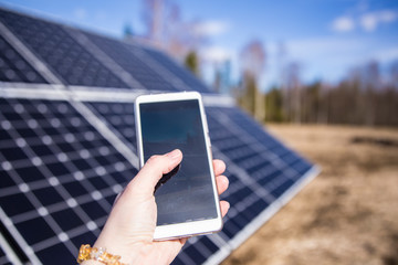 Person looking smartphone screen outdoors on field with solar panels station farm on background....