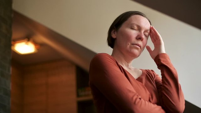 Woman with migraine headache standing by the kitchen loft window