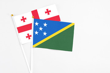 Solomon Islands and Georgia stick flags on white background. High quality fabric, miniature national flag. Peaceful global concept.White floor for copy space.