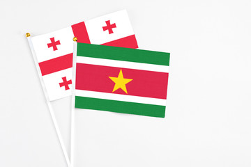 Suriname and Georgia stick flags on white background. High quality fabric, miniature national flag. Peaceful global concept.White floor for copy space.