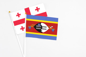 Swaziland and Georgia stick flags on white background. High quality fabric, miniature national flag. Peaceful global concept.White floor for copy space.