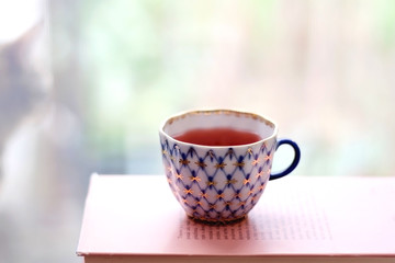 Tea in a vintage porcelain cup on stack of pastel colored books. Selective focus.