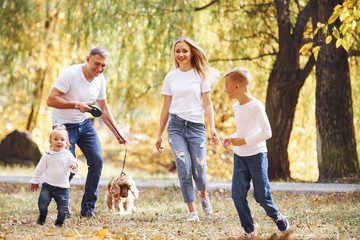 Naklejka na ściany i meble Cheerful young family have a walk in an autumn park together