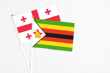 Zimbabwe and Georgia stick flags on white background. High quality fabric, miniature national flag. Peaceful global concept.White floor for copy space.
