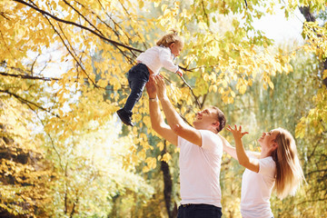 Dad and mother holds theirs daughter in hands and have fun in the autumn park