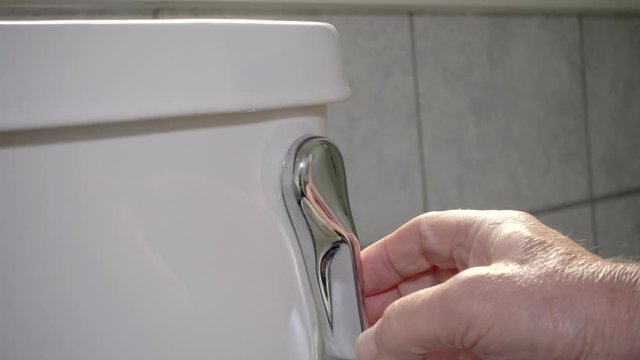 Slow motion close POV shot of a man's hand flushing a toilet.