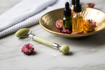 Obraz na płótnie Canvas Massage Steinroller mit Naturkosmetik Beauty Öl Serum Flaschen an Handtuch, Gold Metall Schale und getrocknete Blüten 