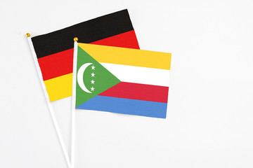 Comoros and Germany stick flags on white background. High quality fabric, miniature national flag. Peaceful global concept.White floor for copy space.