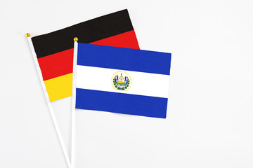 El Salvador and Germany stick flags on white background. High quality fabric, miniature national flag. Peaceful global concept.White floor for copy space.