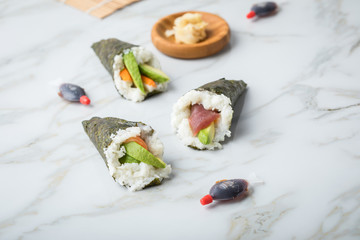 Lachs, Tunfisch und Surimi Avocado Temaki Sushi, eingelegter Ingwer mit Soja Soße Fische und Sushimatte auf Marmor Hintergrund
