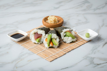 Lachs Fisch, Tunfisch und Surimi Avocado Temaki Sushi, eingelegter Ingwer mit Soja Soße und Sushimatte auf Marmor Hintergrund