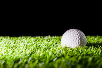 Golf ball on green grass and black background