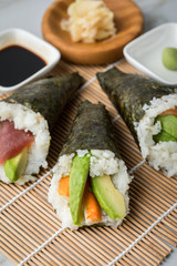 Lachs Fisch, Tunfisch und Surimi Avocado Temaki Sushi, eingelegter Ingwer mit Soja Soße und Sushimatte auf Marmor Hintergrund