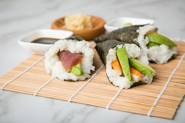 Lachs Fisch, Tunfisch und Surimi Avocado Temaki Sushi, eingelegter Ingwer mit Soja Soße und Sushimatte auf Marmor Hintergrund