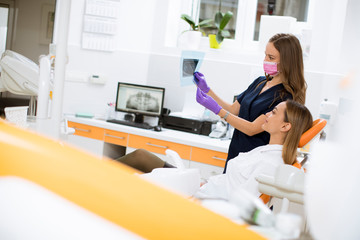 Young female doctor with protective gloves examining radiograph with her patient in the dentist office