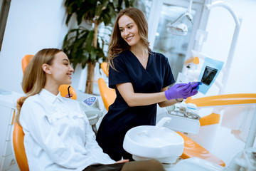 Obraz premium Young female doctor with protective gloves examining radiograph with her patient in the dentist office