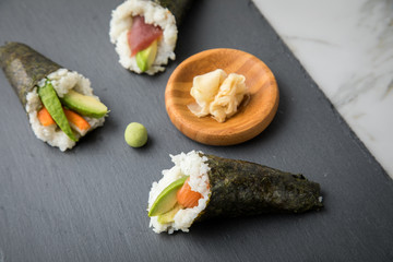 Lachs Fisch, Tunfisch und Surimi Avocado Temaki Sushi, eingelegter Ingwer und Wasabi auf Schiefer Platte und Marmor Hintergrund