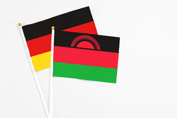 Malawi and Germany stick flags on white background. High quality fabric, miniature national flag. Peaceful global concept.White floor for copy space.
