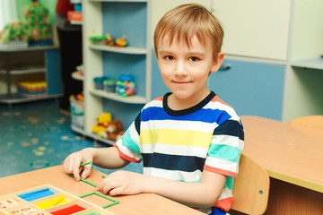 Happy boy sits at the desk at classroom. Kid using colorful sticks and learning counting. Education, development and school concept
