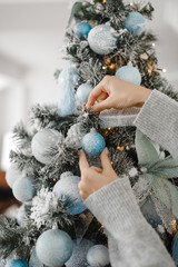 Close up image of woman in sweater decorating Christmas tree with baubles