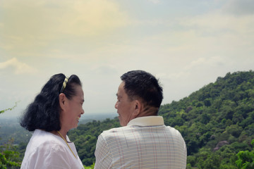 Fototapeta premium Happy Asian elder couple husband and wife standing in the green nature looking and laughing together over sky, loving retirement concept.