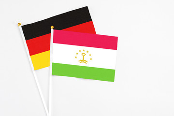 Tajikistan and Germany stick flags on white background. High quality fabric, miniature national flag. Peaceful global concept.White floor for copy space.