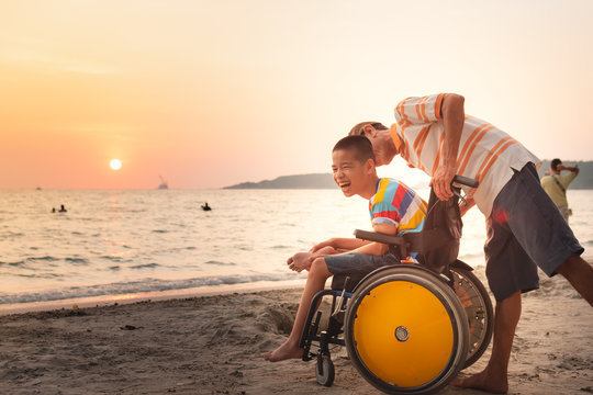 Asian special child on wheelchair is happily on the beach with father,Dad and son spend holiday to travel and learning about nature around the sea,Life in the education age,Happy disabled kid concept.