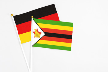 Zimbabwe and Germany stick flags on white background. High quality fabric, miniature national flag. Peaceful global concept.White floor for copy space.