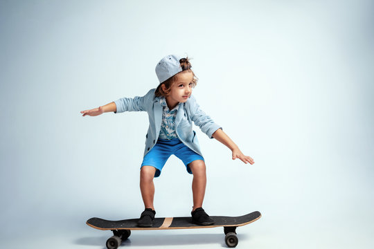 Pretty young boy on skateboard in casual clothes on white studio background. Riding and looks happy. Caucasian male preschooler with bright facial emotions. Childhood, expression, having fun.