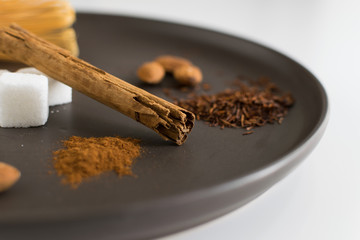 Close-up of ingredients for tea preparation. Cinnamon stick, sugar and almonds on a dark plate. Infusion, hot drink and breakfast concept.