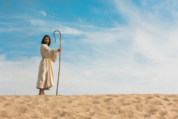 jesus holding wooden cane against blue sky in desert