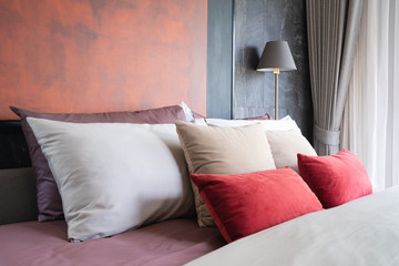 Beautiful group of modern brown, red, beige colors fabric pillows on the brown bed with beige...