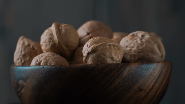A bowl of walnuts revolves on a dark background. Close-up.