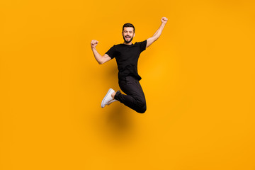 Fototapeta na wymiar Full body photo of handsome excited guy jumping high raising fists celebrating football team goal supporting fan wear black t-shirt pants isolated yellow color background