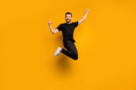 Full body photo of handsome excited guy jumping high raising fists celebrating football team goal supporting fan wear black t-shirt pants isolated yellow color background