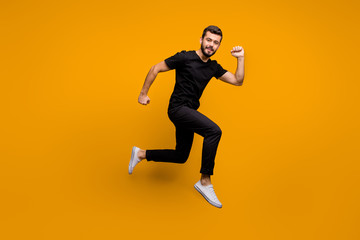 Fototapeta na wymiar Full length profile photo of handsome millennial guy jumping high rush shopping mall black friday offers season wear black t-shirt pants isolated yellow color background