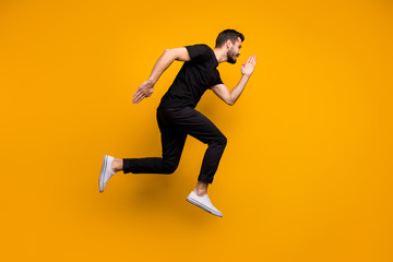 Fototapeta na wymiar Full body profile photo of handsome millennial guy jumping high rushing low prices discount shopping mall wear black t-shirt trousers isolated yellow color background