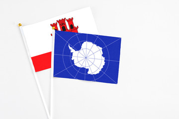 Antarctica and Gibraltar stick flags on white background. High quality fabric, miniature national flag. Peaceful global concept.White floor for copy space.