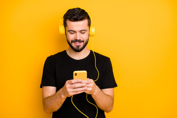 Portrait of positive cheerful guy listen music use yellow headset search song on his cellphone want choose sound track wear casual style clothing isolated over bright color background