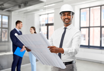 architecture, construction business and occupation concept - smiling indian male architect in helmet with blueprint over people in empty office room background