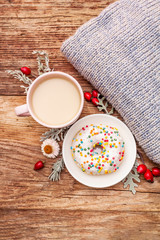 Hot coffee with a donut. Autumn drink for a good mood with plaid, fresh rose hips, leaves and flowers. Old wood plank background