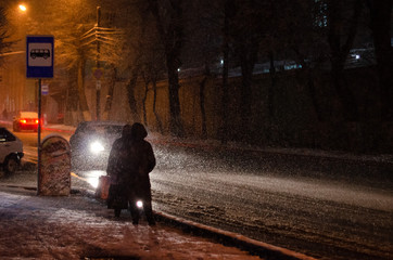 People waiting for a bus at a stop in a winter blizzard