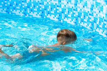 Unrecognizable Child learn to swim, dive in blue pool with fun - jumping deep down underwater with splashes.