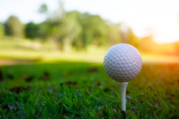 Golf ball on tee in beautiful golf course at sunset background.