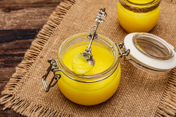 Pure or desi ghee (ghi), clarified melted butter. Healthy fats bulletproof diet concept or paleo style plan. Glass jar, silver spoon on vintage sackcloth. Wooden boards background