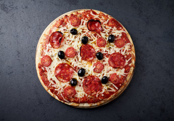 Pizza with chorizo, mozzarella cheese, cherry tomatoes, black olives and oregano. Home made food. Concept for a tasty and hearty meal. Black stone background. Top view. 