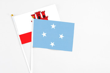 Micronesia and Gibraltar stick flags on white background. High quality fabric, miniature national flag. Peaceful global concept.White floor for copy space.