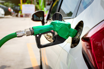 White car refueling at gas station with green fuel nozzle.