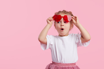 Portrait of surprised cute little toddler girl in the heart shape sunglasses. Child with open mouth...
